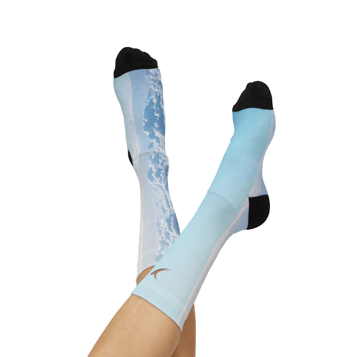 Nurse Crew Socks in light blue and white — blue sky cloud print with black toe and heel, small terracotta bird at the cuff — worn view with feet raised