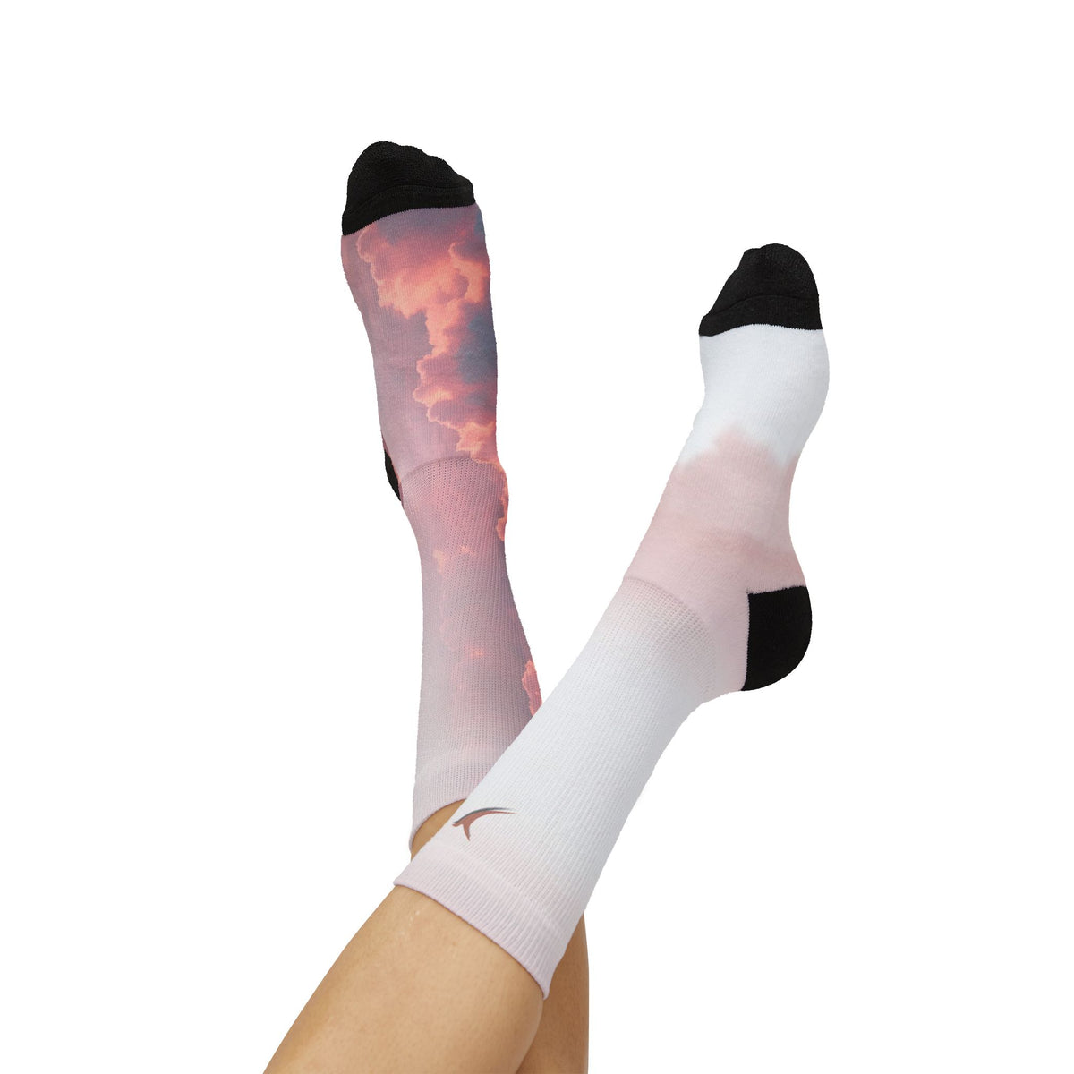 Nurse Crew Socks in blush pink and white — pink sunset cloud print with black toe and heel, terracotta bird at the cuff — worn view with feet raised